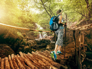 Hiking. Woman hikers walking on a bridge on the forest in the mountains on the waterfall. Girl with a backpack and sneakers traveling outdoors. Adventure in a hike.