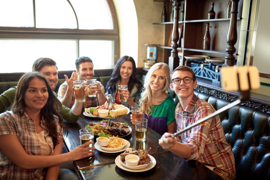 happy friends with selfie stick at bar or pub