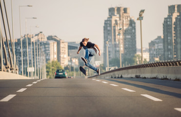 Skater doing tricks and jumping on the street highway bridge, through urban traffic. Free riding skateboard