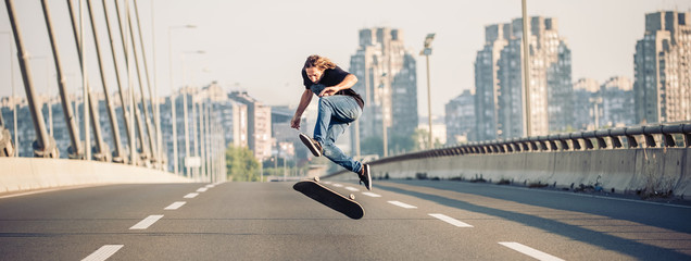 Skater doing tricks and jumping on the street highway bridge, through urban traffic. Free riding...