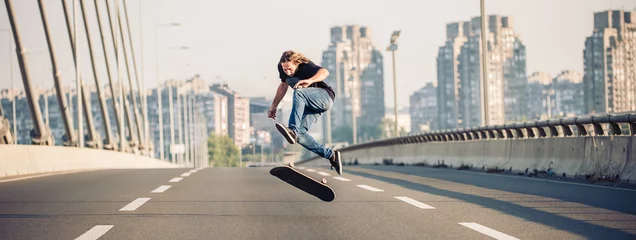 Deurstickers Skater doing tricks and jumping on the street highway bridge, through urban traffic. Free riding skateboard. Panorama view © guruXOX