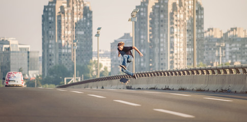 Skater doing tricks and jumping on the street highway bridge, through urban traffic. Free riding skateboard. Panorama view © guruXOX