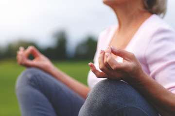 Hands of mature woman practicing yoga at lotus pose, outdoors