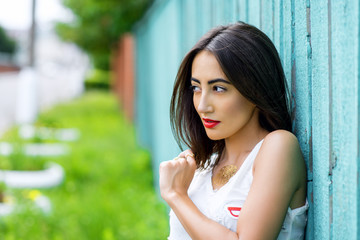 Girl brunette in a park in the summer resting white blouse on the background of  wooden fence, fashion lifestyle, gentle look. Sensual make-up, tanned skin and bright red lipstick.