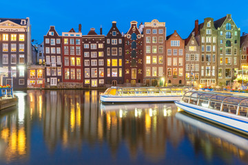 Fototapeta na wymiar Beautiful typical Dutch dancing houses and tourist boats at the Amsterdam canal Damrak at night, Holland, Netherlands.