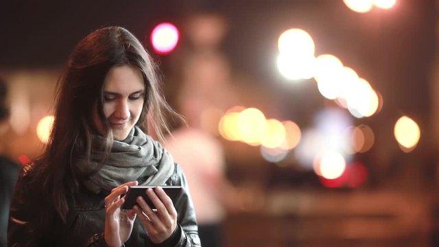 Pretty young woman using her smartphone at night. Lady in the street in cold weather. Modern technology.
