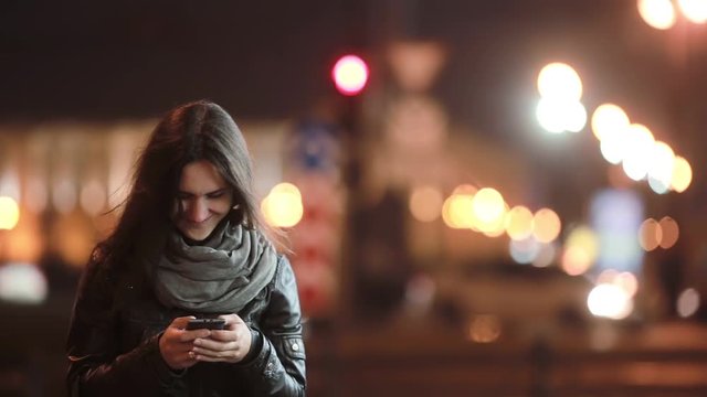 Pretty young woman walking in the street, slowly getting in focus. Smiling lady using her smartphone. Modern technology