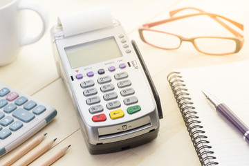 Credit Card Terminal or EDC on cashier wooden table in the store with credit card, pen, calculator and glasses on background.