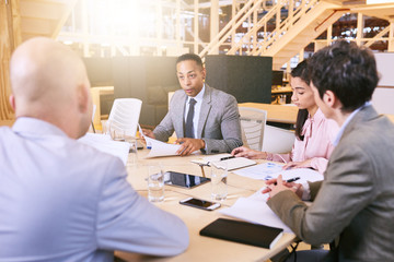 Indoor meeting between 4 business executives in a warm creative environment, making use of tech and documents during the early hours of the morning in preparation for the coming week.