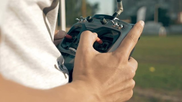 Close up of hands holding a transmitter and controlling FPV drone. Drone control training process in sunny day. Quadrocopter competitions outdoors.