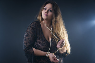 Young naked beautiful caucasian plus size model, xxl woman in black peignoir on smoky background,...