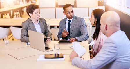 Business meeting between four executives in modern office space with both male and female employees participating in the decision making process.
