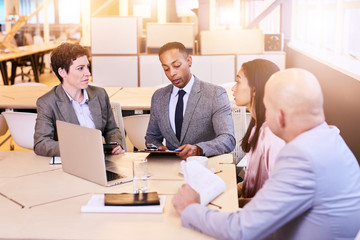 Business meeting between four executives in modern office space with both male and female employees participating in the decision making process.