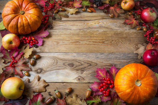 Frame of pumpkins, apples, acorns, berries and fall leaves on wo