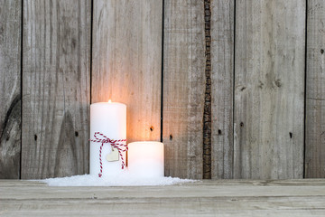 White candles in snow by wood background