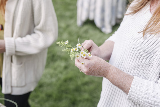Close up of a woman, standing in a garden, making a flower wreath.