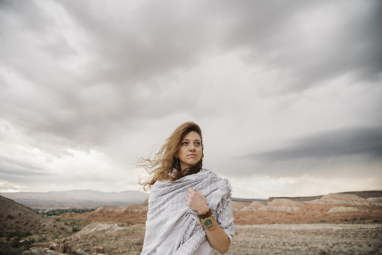 A woman with windblown hair wrapped in a shawl in a desert landscape