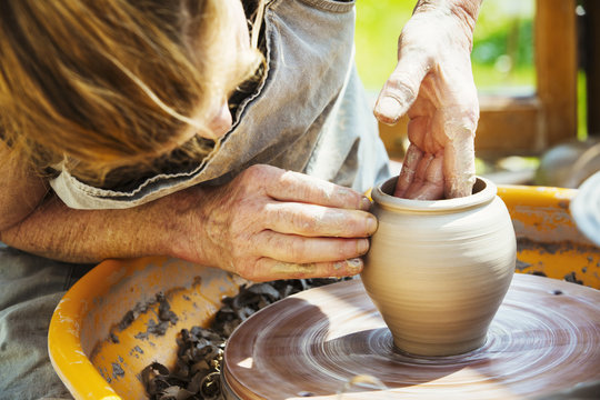 A woman potter working clay on a potter's wheel in her workshop. 