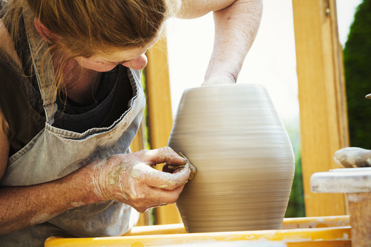 A woman potter working clay on a potter's wheel in her workshop. 