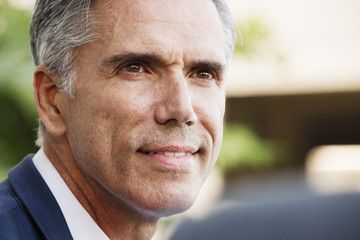 A man in a white shirt with grey hair, smiling, his head turned to speak to another person.