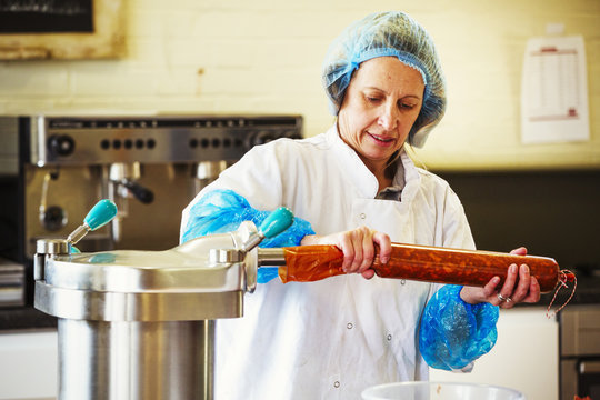 Woman working in a butchery, wearing protective clothes and gloves, filling a casing with Chorizo sausage meat.