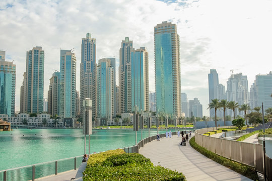 People walking along the waterfront promenade that runs along the Burj Khalifa Lake and the Burj Khalifa. On background, the Old Town Island and the Dubai Mall in Downtown Dubai.