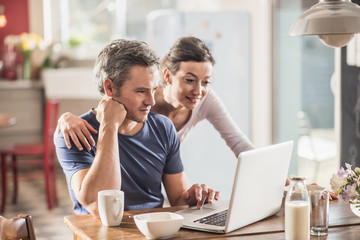 A couple using a laptop while having breakfast in the kitchen