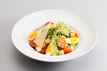 Caesar salad with shrimp tomato cherry, eggs. white plate gray background. horizontal photo