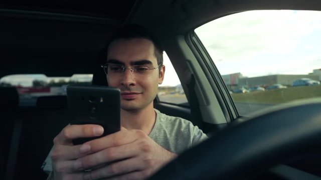 Young man in a stopped vehicle using his smartphone to text a message.
