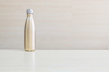 Closeup gold color of aluminium flask for keep hot water on blurred wooden desk and wall textured background under window light