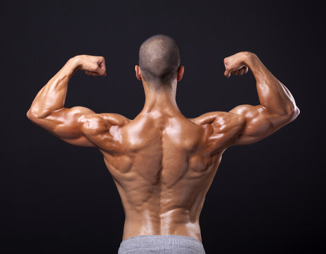 Back view of a male bodybuilder flexing his biceps on black back