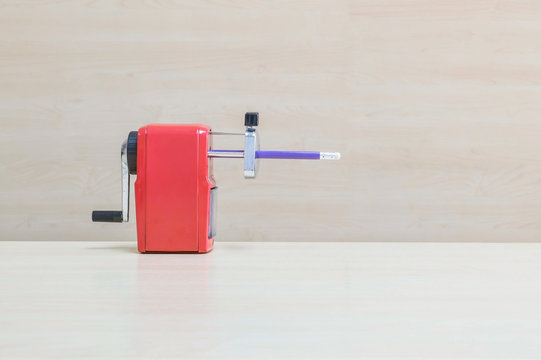 Closeup old red pencil sharpener with purple pencil on wood desk and wall in work room textured background under window light