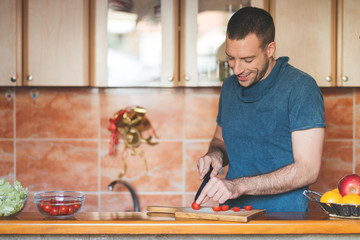 Happy man in kitchen making vegetable salad.