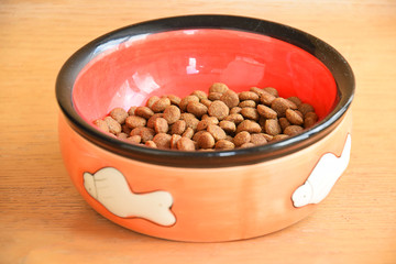 Dry cat food in bowl on wooden background