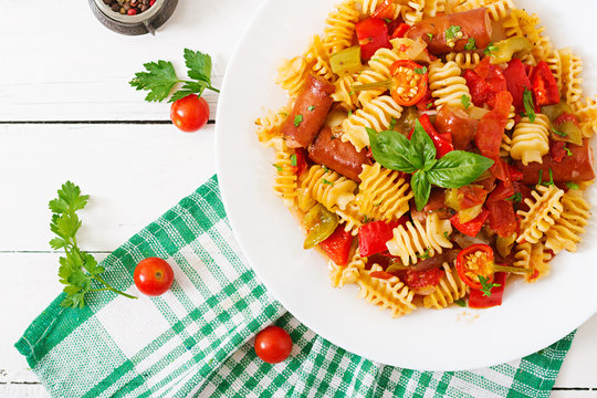Pasta with tomato sauce with sausage, tomatoes, green basil decorated in white plate on a wooden background. Top view