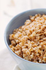 spelt in blue bowl on white wooden background