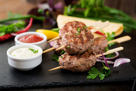 Appetizing kofta kebab (meatballs) with sauce and tortillas tacos on black background