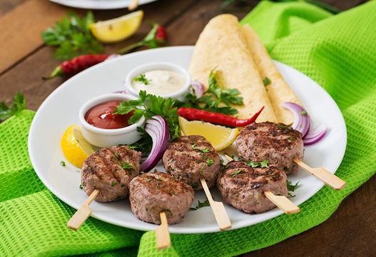 Appetizing kofta kebab (meatballs) with sauce and tortillas tacos on a white plate