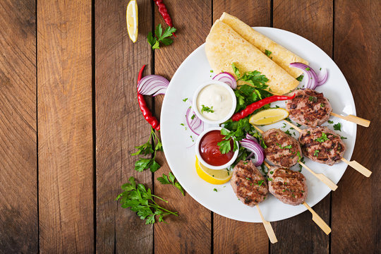Appetizing kofta kebab (meatballs) with sauce and tortillas tacos on a white plate. Top view
