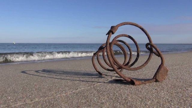 Old rusted iron spring on the sand by the sea