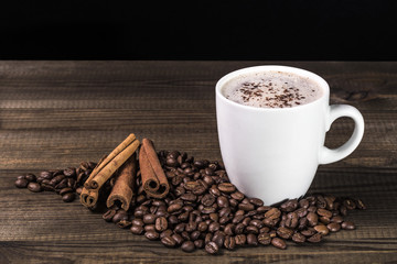 cup of coffee with coffee beans and cinnamon on wooden table. Image with copy space