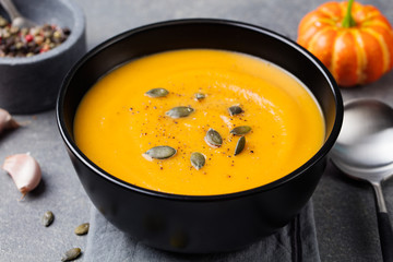 Pumpkin cream soup with pumpkin seeds in a black bowl. Grey stone background.