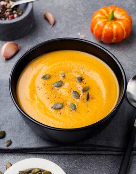 Pumpkin cream soup with pumpkin seeds in a black bowl. Grey stone background.