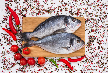 Raw dorado fish on wooden cutting board with vegetables. Top view, copy space 