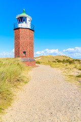 Fototapeta na wymiar Lighthouse on sand dune against blue sky with white clouds on northern coast of Sylt island near Kampen village, Germany