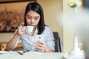Young woman using smartphone with a coffee cup and notebook.