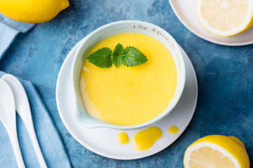 Lemon curd in ceramic bowl with fresh lemons on a blue napkin background. Top view. Selective focus