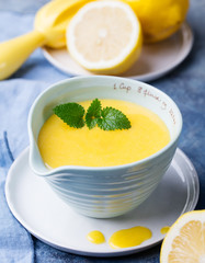 Lemon curd in ceramic bowl with fresh lemons on a blue napkin background. Selective focus