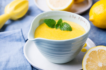 Lemon curd in ceramic bowl with fresh lemons on a blue napkin background. Selective focus