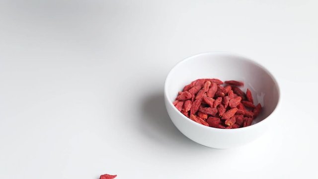 Putting goji berries - Lycium barbarum - in a bowl. White background. Goji berries from south China -  whole fruit or its extracts are said to have numerous implied health effects. 